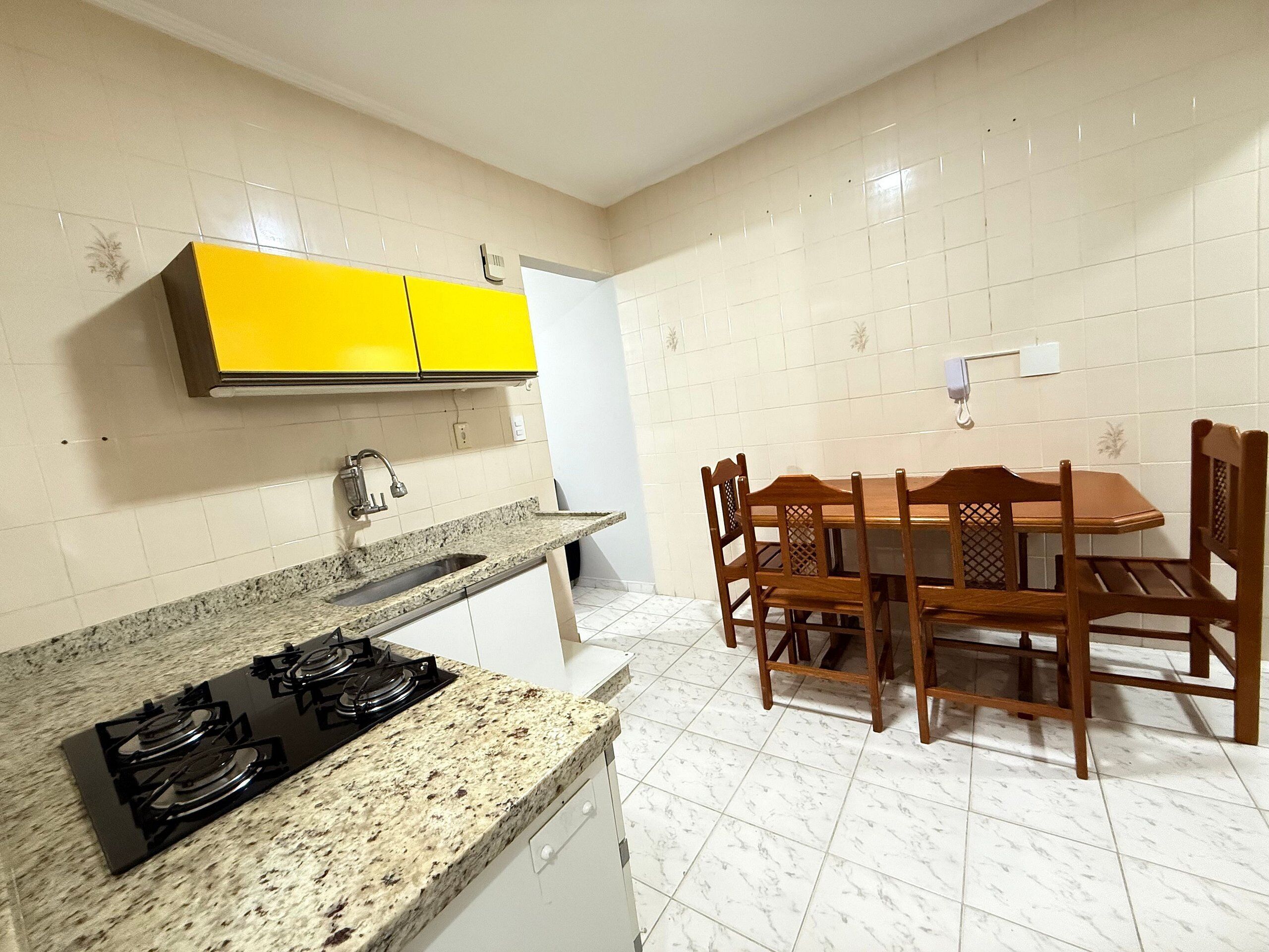 A kitchen with a granite countertop, a gas stove, yellow cabinets, and a dining table with wooden chairs.