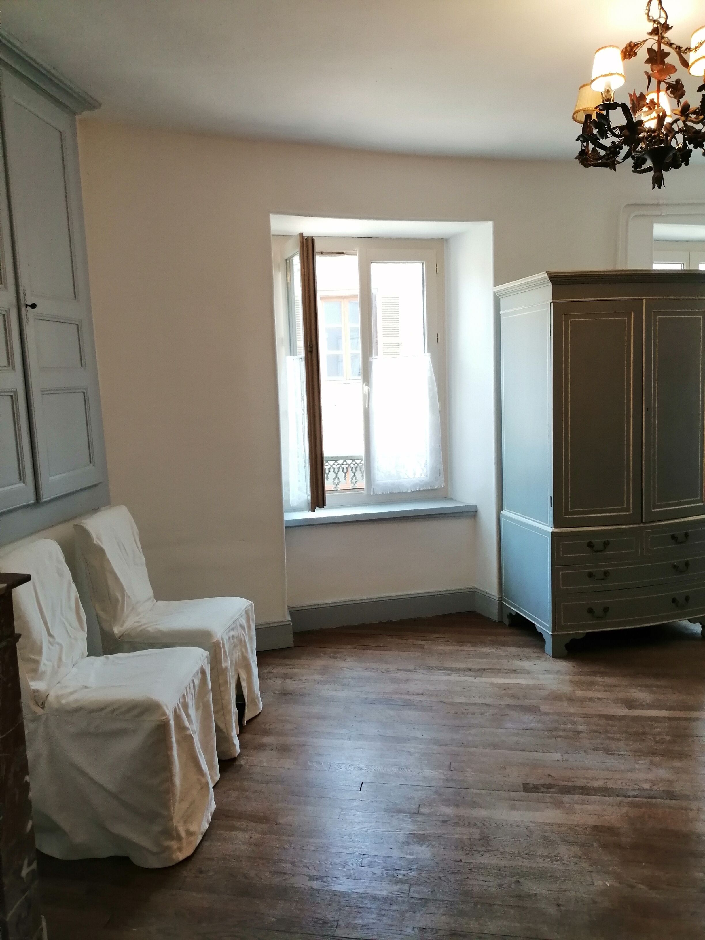 A room with a large window, a wooden floor, and a wardrobe.