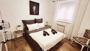 A bedroom with a bed, a chair, a radiator, a window with curtains, and a framed picture on the wall.