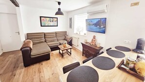 A modern living room with a sectional sofa, a coffee table, a TV, and a dining area with a wooden table and chairs.