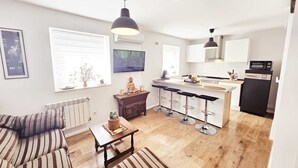 A modern kitchen with a central island, bar stools, and a dining area with striped sofas.