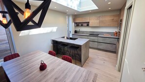 Una cocina moderna con una isla central, taburetes de bar y una mesa de comedor con hervidor.