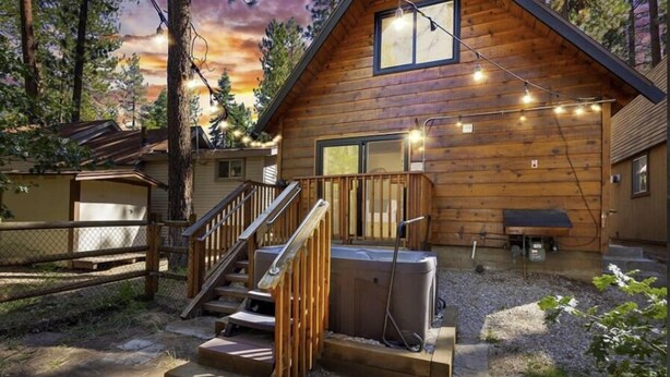 Una cabaña de madera con un jacuzzi, mobiliario exterior y una escalera que lleva a una terraza.