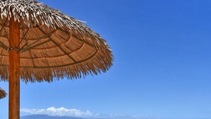 A beachside patio with a table and chairs under a thatched umbrella, overlooking the ocean. - West Maui Ocean View Corner 2BR with Pool + AC (Lahaina)