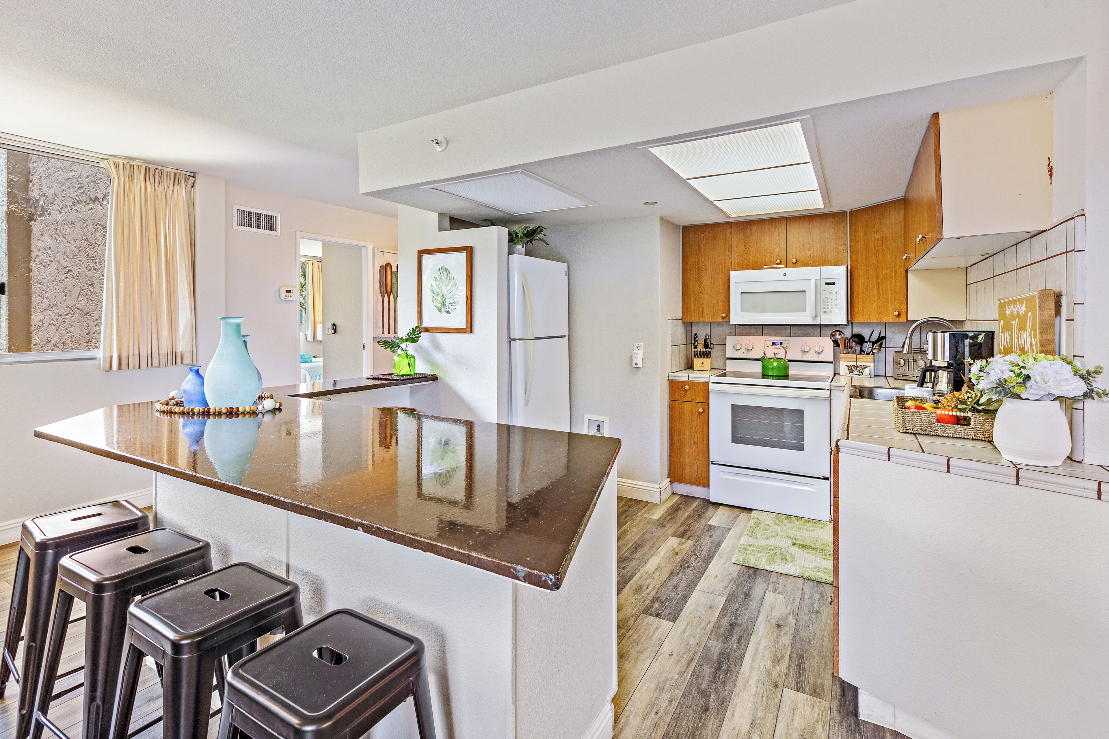 A modern kitchen with a central island, bar stools, a microwave, oven, and a refrigerator.