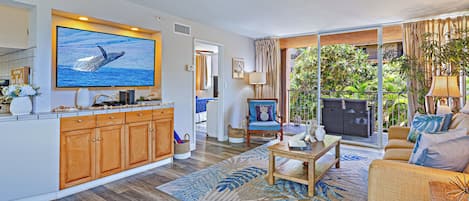 A spacious living area with a large flat-screen TV, wooden cabinets, a sofa, and a dining table.
