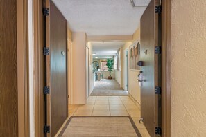 A hallway with wooden doors, a carpeted floor, and a view into a dining area with a plant and table. - Ocean Breeze at Jazz -Cozy 2BR/2BA, View, Pool, AC, Beach Access &Top Location (Lahaina)