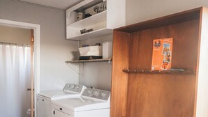 Un lavadero con lavadora y secadora, estanterías de madera y un ventilador de techo.