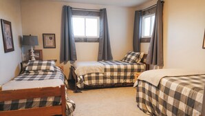 Una habitación con tres camas, cada una con ropa de cama a cuadros, una lámpara y cuadros enmarcados en la pared.