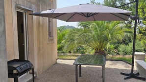 Un patio al aire libre con una parrilla, una mesa y una sombrilla.