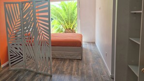 Un dormitorio con una cama, un separador decorativo y vista a una planta a través de una ventana.