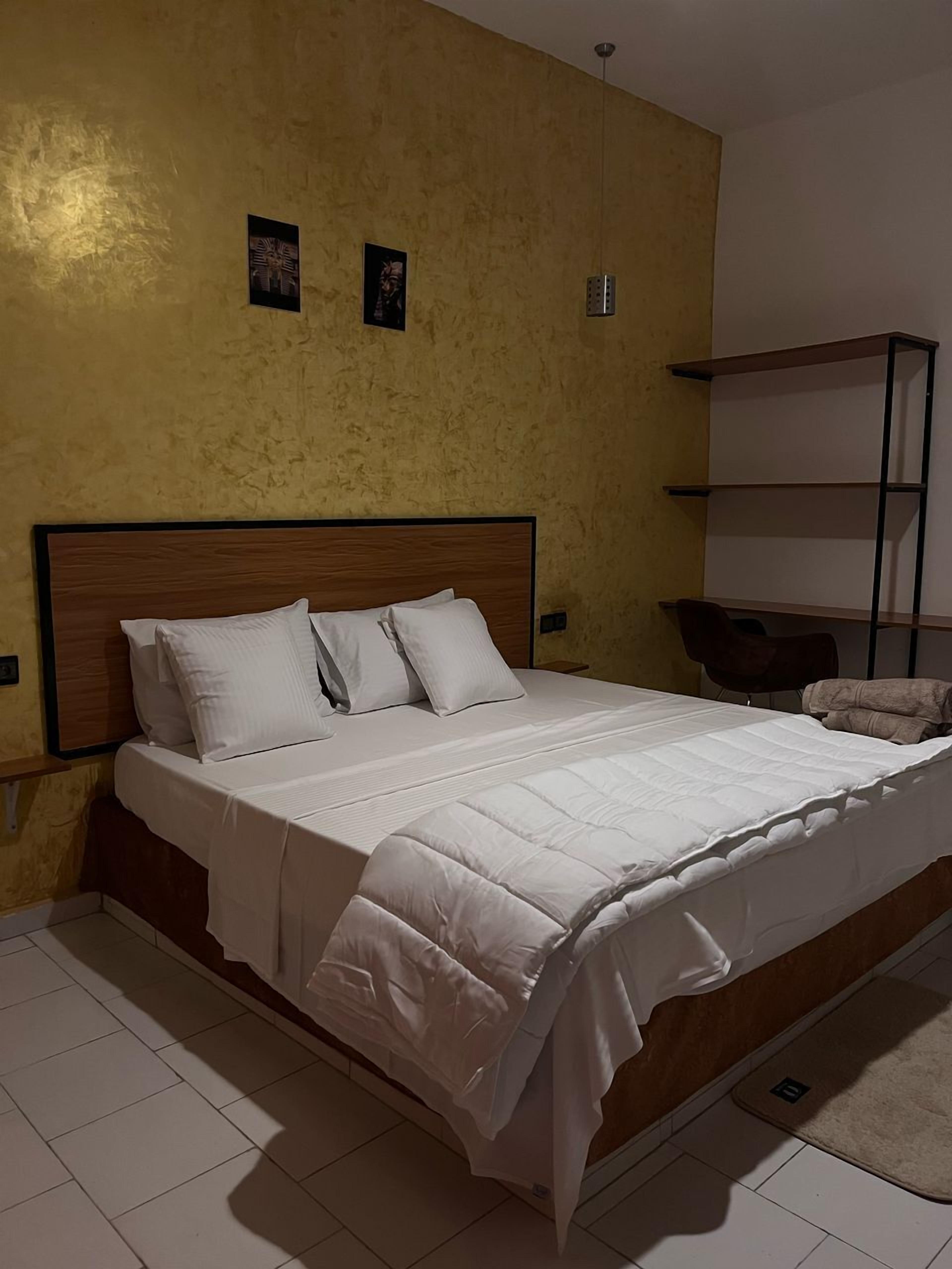 A neatly made bed with white bedding in a room with yellow walls and a wooden headboard.