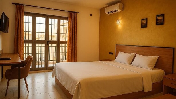A hotel room with a bed, a desk, a chair, and a window with curtains. - Hotel KEUR HORUS (St. Louis)