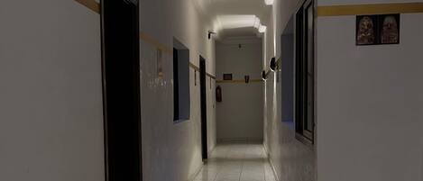 A long, narrow hallway with white walls and tiled floors. There are doors on both sides, and a sign prohibiting smoking and vaping is visible on the right wall.