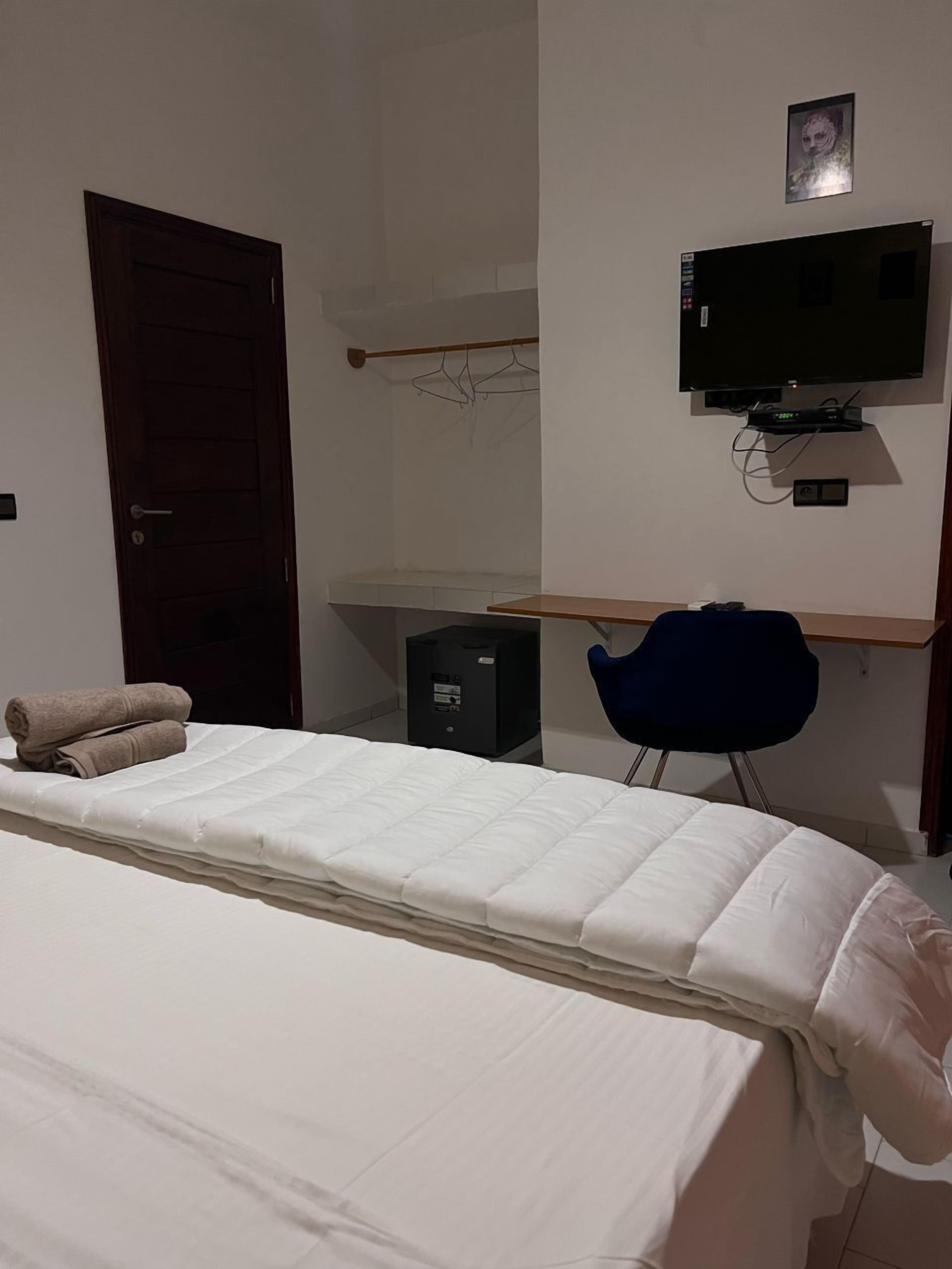 A bedroom with a bed, a desk, a chair, a TV, and a wardrobe.