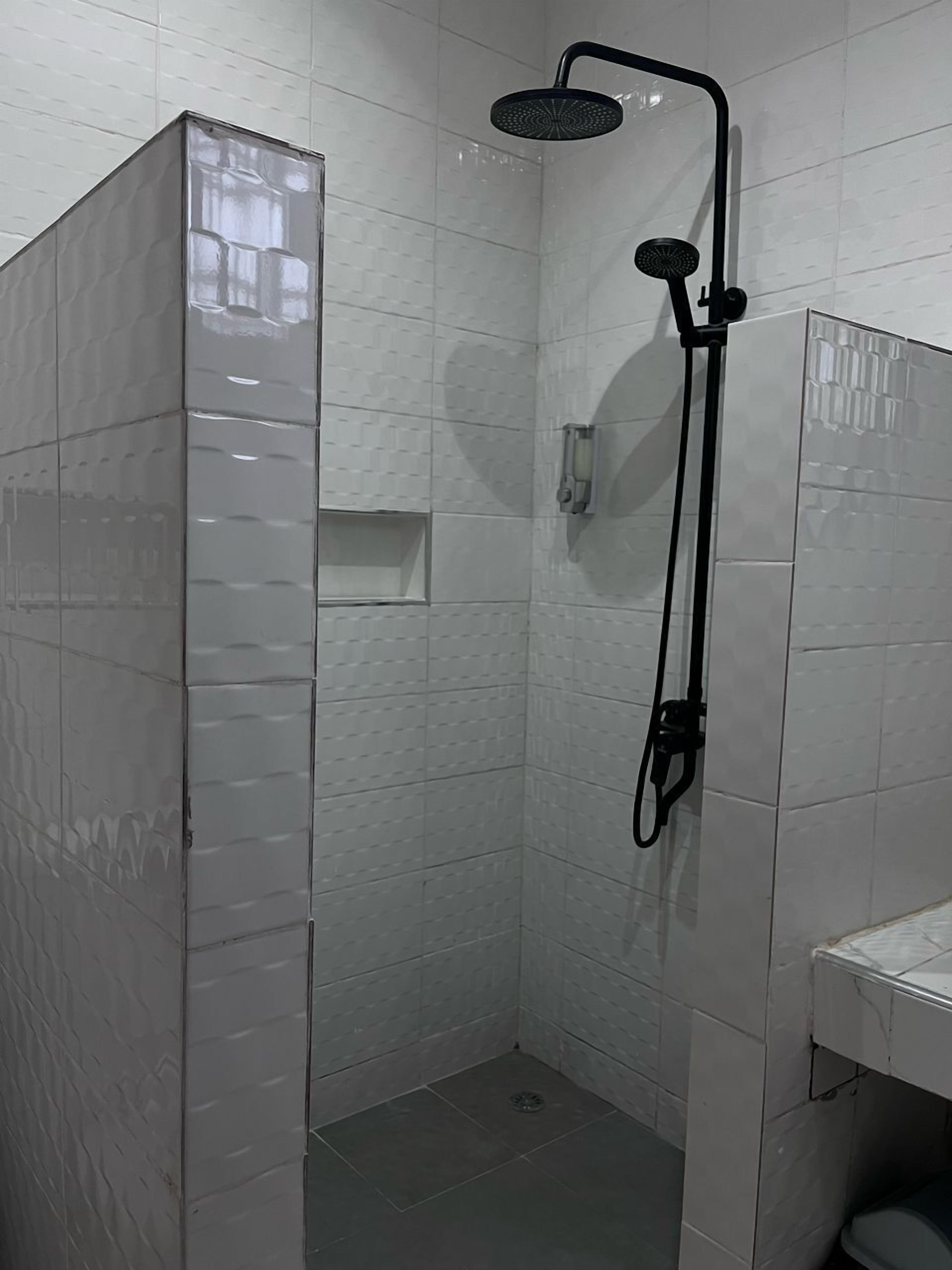 Pequeno espaço de duche fechado, com paredes revestidas a azulejos brancos e um chuveiro preto.