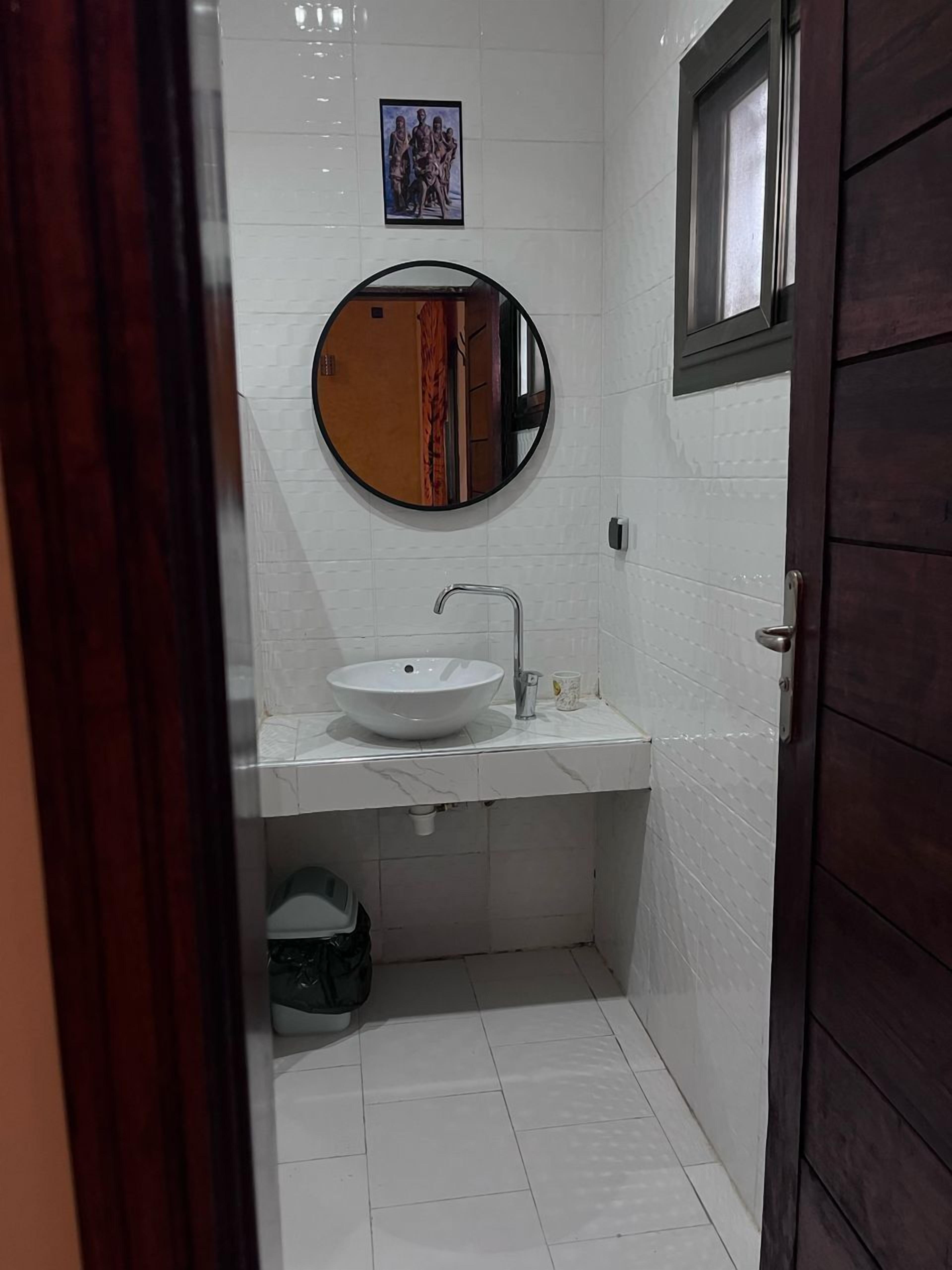 A small bathroom with a round mirror, a white sink, and a window.