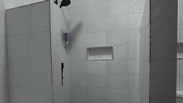 Un baño moderno con baldosas de mármol blanco, cabina de ducha de vidrio y tocador empotrado.