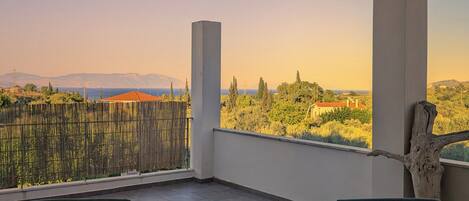 A balcony with two wicker chairs, a small wooden table, and a view of a mountainous landscape.