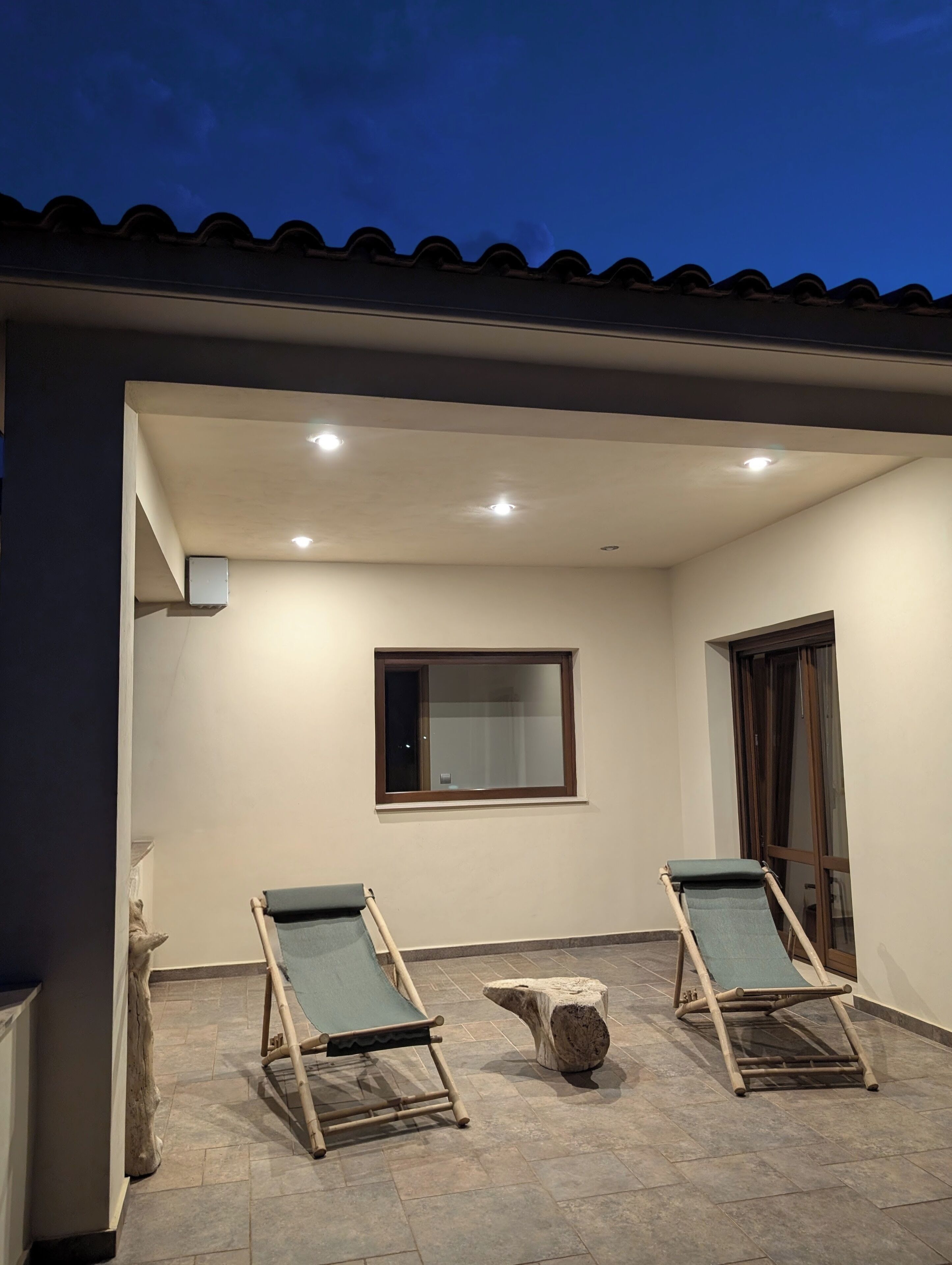 Un patio techado con dos sillones, una mesita y una ventana.