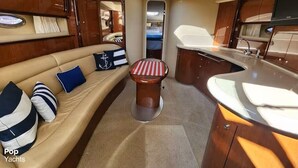 Interior de un yate con un sofá, una mesita redonda y una zona de cocina.