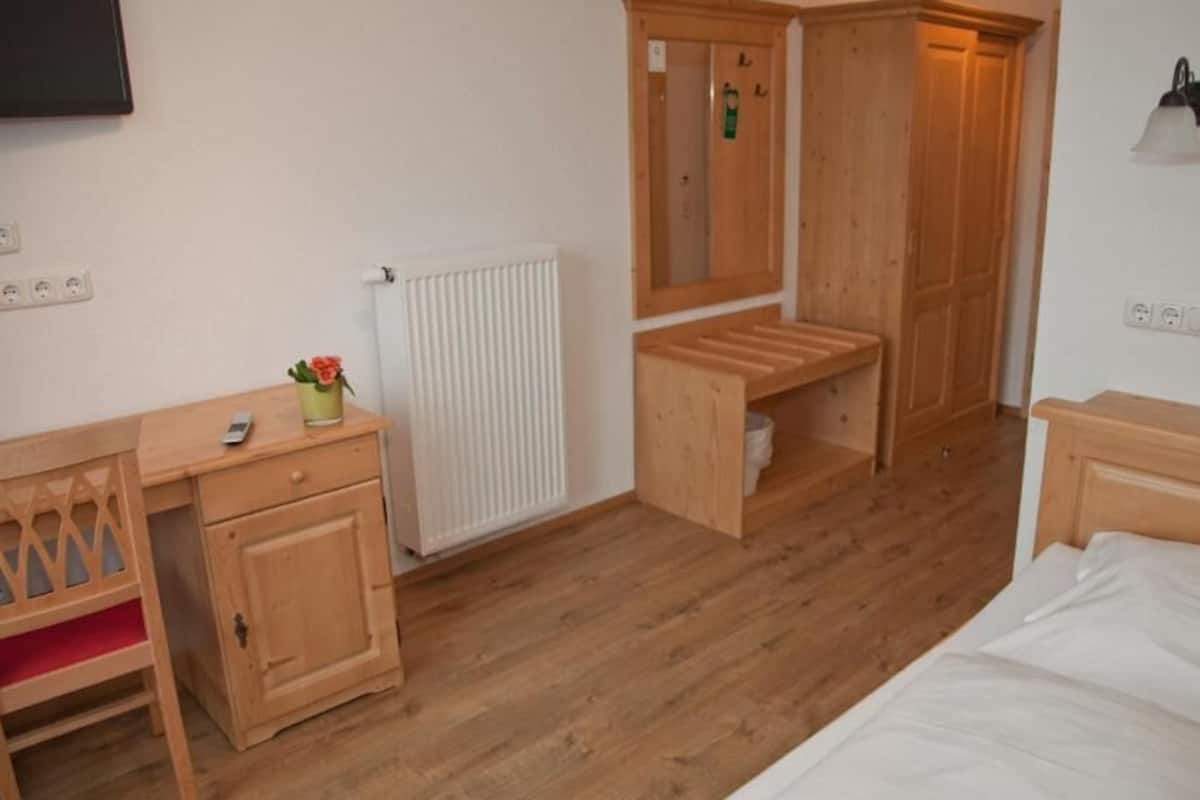 Une chambre à coucher avec un lit en bois, un bureau avec une chaise, un radiateur et une armoire en bois.