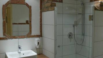 Un baño con lavamanos blanco, un espejo y cabina de ducha con mampara de vidrio.