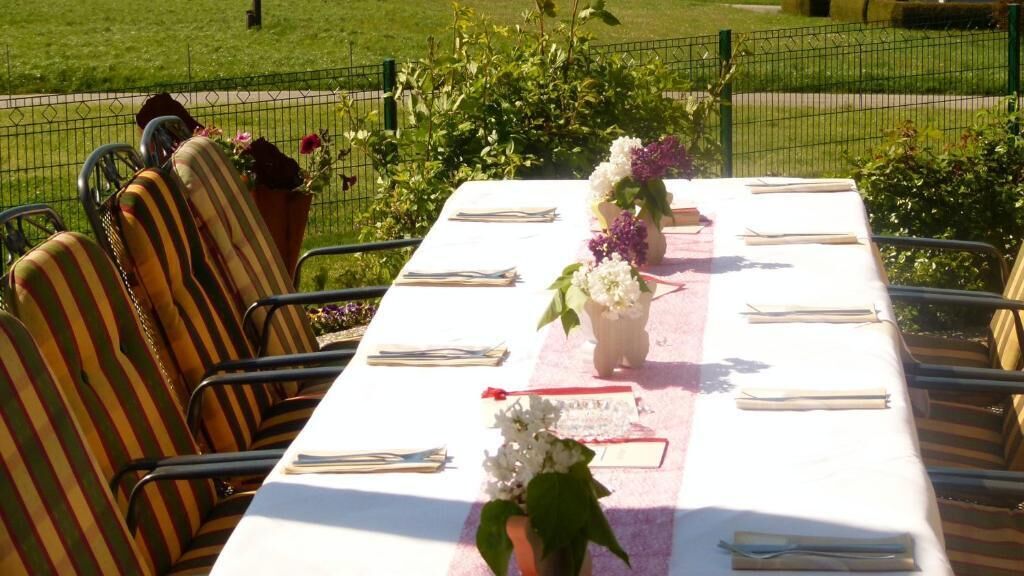 Un tavolo apparecchiato all'aperto con sedie a righe, una tovaglia bianca e centrotavola floreali.
