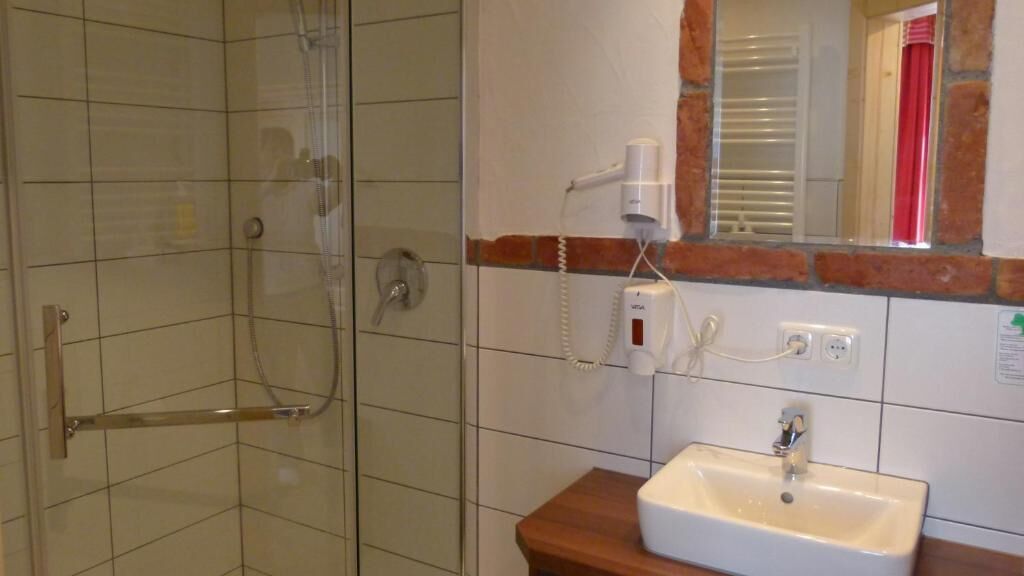 A bathroom with a glass-enclosed shower, a white sink, and a mirror with a red curtain.