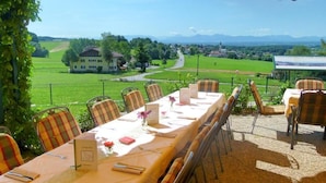 Une longue table à manger, dressée pour six personnes, avec des chaises à rayures, donnant sur un paysage verdoyant, et un panneau visible au fond.