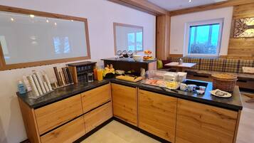 A modern kitchen with wooden cabinets, a black countertop, and a breakfast bar. There are various breakfast items and condiments on the counter.