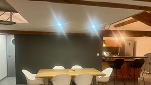 A dining area with a wooden table and white chairs, a dark accent wall, and a kitchen in the background. - Magnificent Loft near town center (Saint-Chamas)