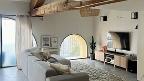 A modern living room with a large sofa, a flat-screen TV, and a wooden ceiling beam. - Magnificent Loft near town center (Saint-Chamas)