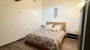 A bedroom with a wooden floor, a bed with floral bedding, a nightstand, and a wall decoration. - Magnificent Loft near town center (Saint-Chamas)