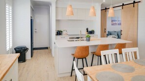 A modern kitchen with white cabinets, a central island, and pendant lighting. There is a dining area with a wooden table and chairs. - Nessie`s Nook Relax in fully Air-Conditioned Style (Dunsborough)
