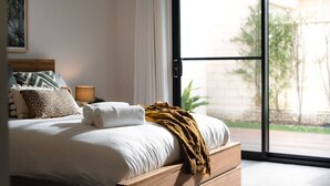 A bedroom with a large window, a bed with white linens, a wooden headboard, and a brown throw blanket. - Mainbreak Dunsborough – Stylish Coastal Retreat (Dunsborough)