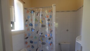 Ein Badezimmer mit Duschvorhang mit Fischmotiven, Toilette und Waschbecken mit Spiegel.