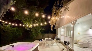 An outdoor hot tub area with string lights, wooden steps, and a covered seating area with white chairs and tables. - Amazing Austin Gataway 6BR4BA: HotTub •Billiards •Patio •Chef Kitchen (Austin)