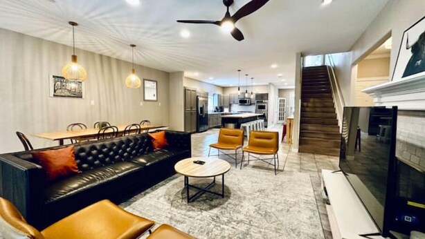 A modern living room with a black leather sofa, two brown leather chairs, a round coffee table, and a TV. There is a kitchen in the background with a dining area. - Amazing Austin Gataway 6BR4BA: HotTub •Billiards •Patio •Chef Kitchen (Austin)