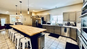 A modern kitchen with a central island, stainless steel appliances, and a dining area with bar stools. - Amazing Austin Gataway 6BR4BA: HotTub •Billiards •Patio •Chef Kitchen (Austin)