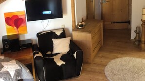 Une pièce chaleureuse avec un plafond en pente, un téléviseur fixé au mur, un canapé en cuir noir, une commode en bois et un tapis rond.