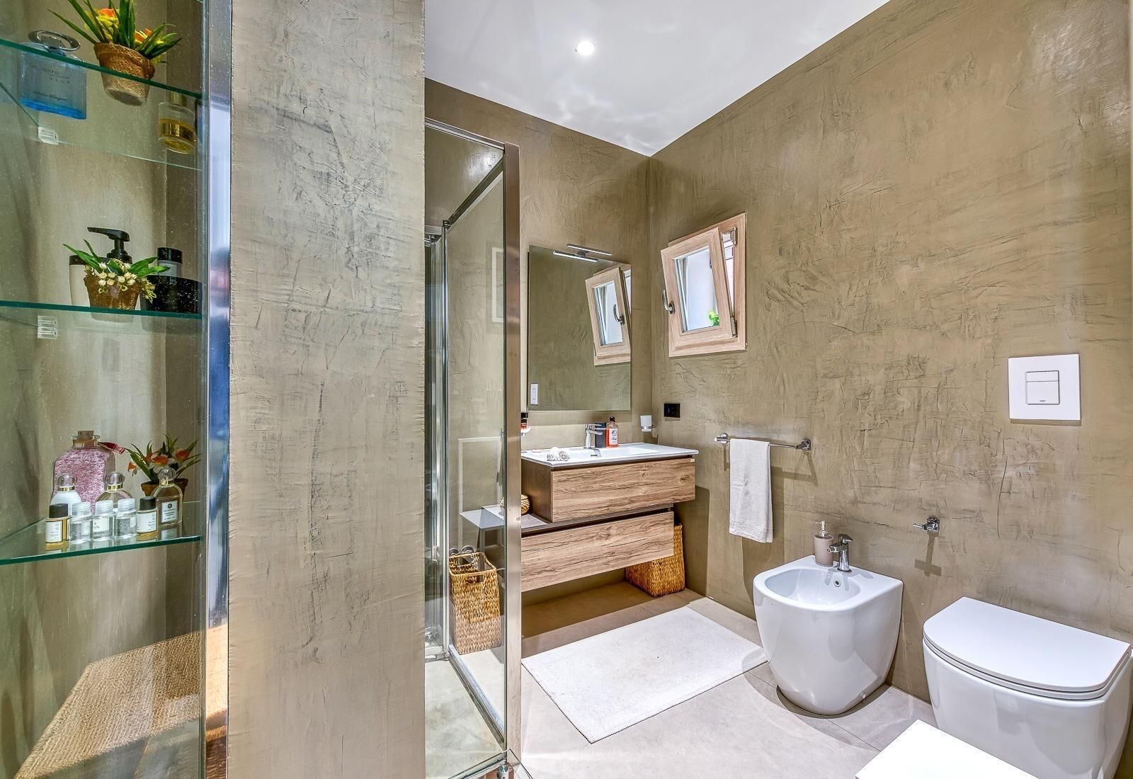 A modern bathroom with a glass shower enclosure, a wooden vanity, a bidet, and a large mirror.