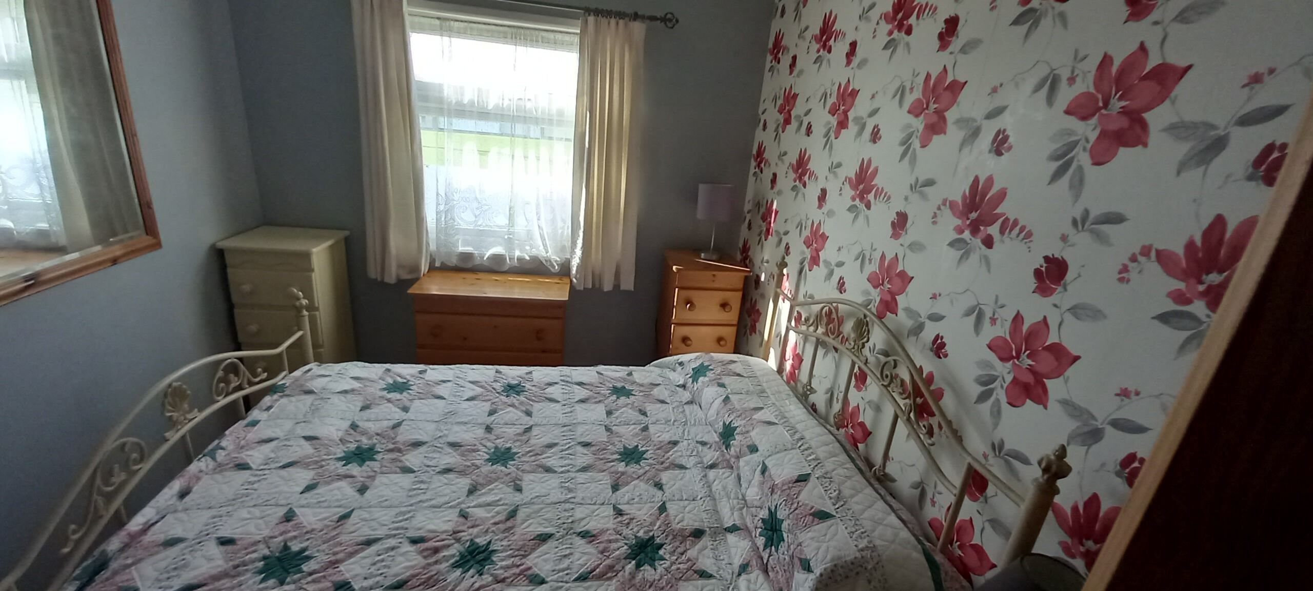 A bedroom with a bed, a dresser, a nightstand, and a window with curtains.