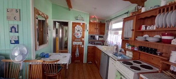 A compact kitchen with wooden cabinets, a sink, a stove, and a fan. - 3 Bed Chalet - Sleeps 6 - Parking - Garden - Wifi (Great Yarmouth)