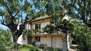 A two-story building with a balcony, surrounded by lush greenery and trees. - Villa Six-Fours (Six-Fours-les-Plages)