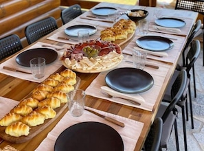 A wooden table set for a meal with plates, cutlery, and a variety of food items including pastries and a charcuterie board.