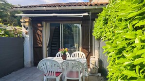 A patio with a table and chairs, a potted plant, and a sliding glass door leading to a covered area.