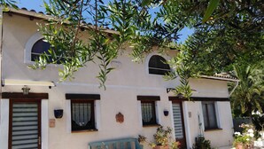 A building with a white facade, multiple windows with shutters, and a bench outside.