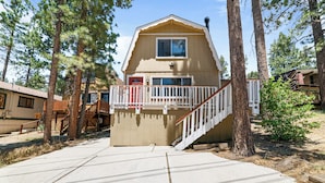 A cabin with a wooden deck, a red door, and a staircase leading to a balcony. - Cabin in the Pines (Big Bear Lake)