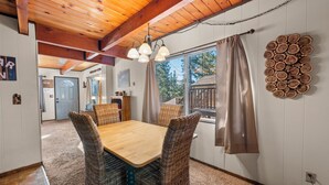 A dining area with a wooden table and wicker chairs, a chandelier, and a log wall decoration. - Cabin in the Pines (Big Bear Lake)